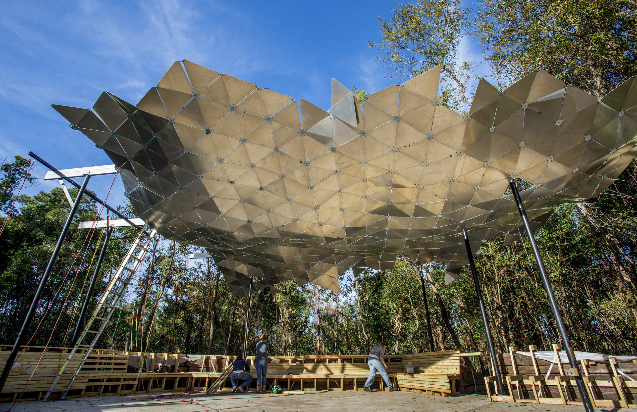 photo of a shaded pavilion with a geometric patterned roof and a wooden deck.